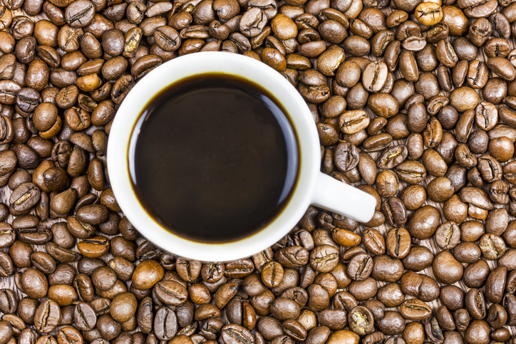 A cup of black coffee surrounded by coffee beans