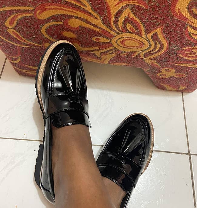 A reviewer photo of a pair of feet wearing the black patent loafers with tassels on the toe 