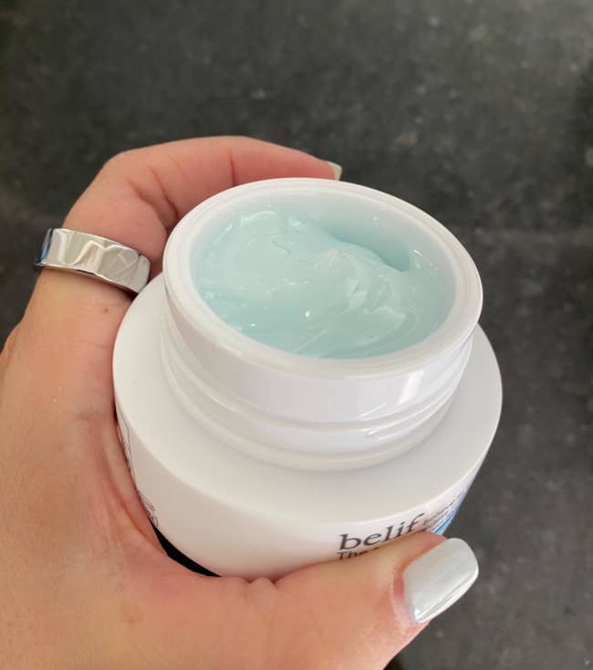 a reviewer showing the jar opened to reveal a light blue cream inside