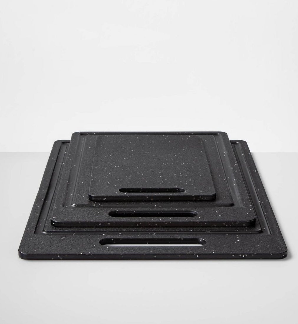 three different sized black with white speckles cutting boards with handles stacked on top of each other