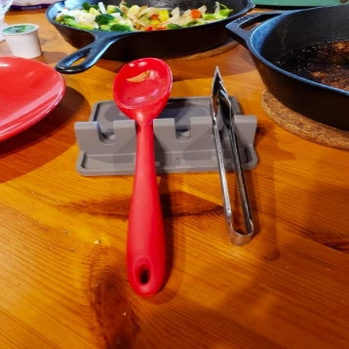 a gray silicone spoon rest with a red spoon and tongs in the slots 