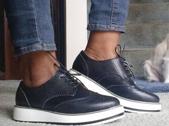 a reviewer photo of someone wearing jeans, the platform oxfords in navy, and a dog in the background 