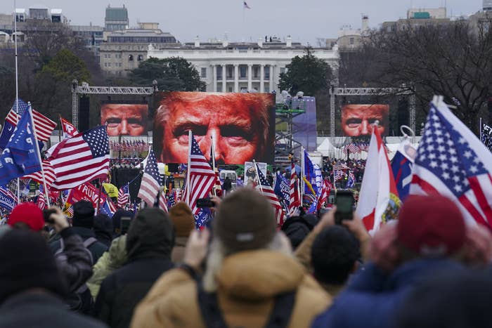 A close-up of Trump&#x27;s eyes appear on three screens in the background before a crowd of people waving US and Trump flags