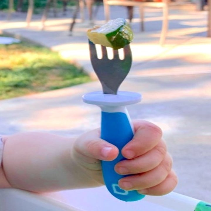 toddler hand holding on to a blue fork with a zucchini on top