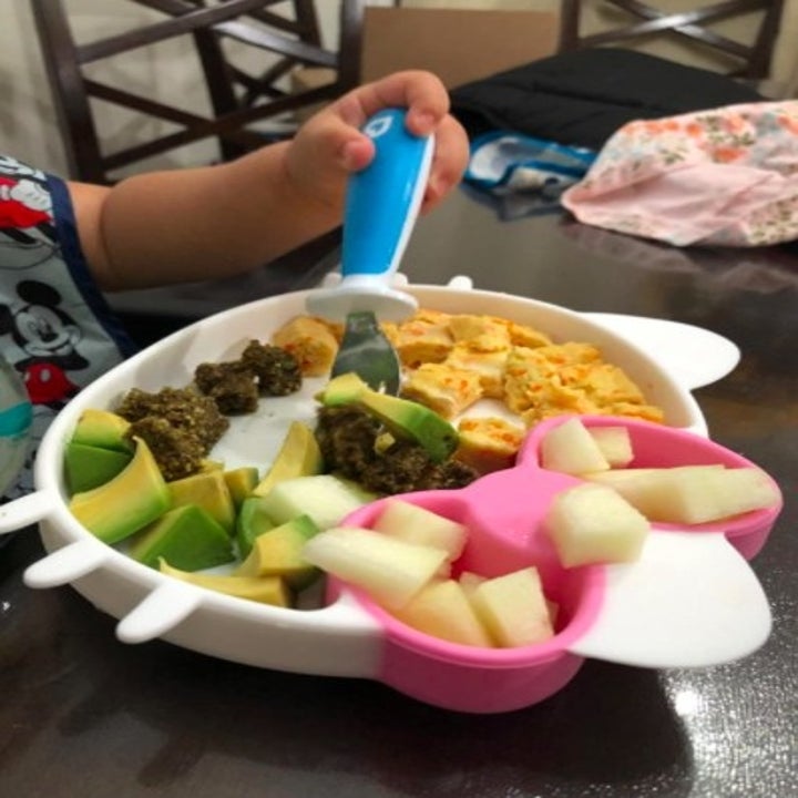 child using a blue utensil to eat avocado