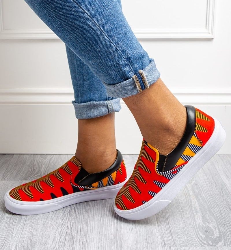 a model wearing jeans and siip-on sneakers with a red and yellow print and white rubber soles 