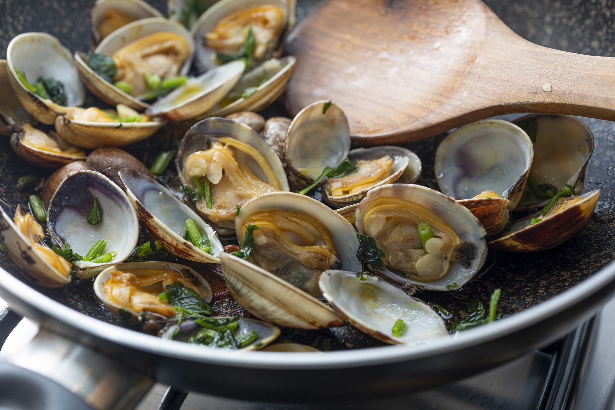 Clams tossed in fresh herbs in a skillet.