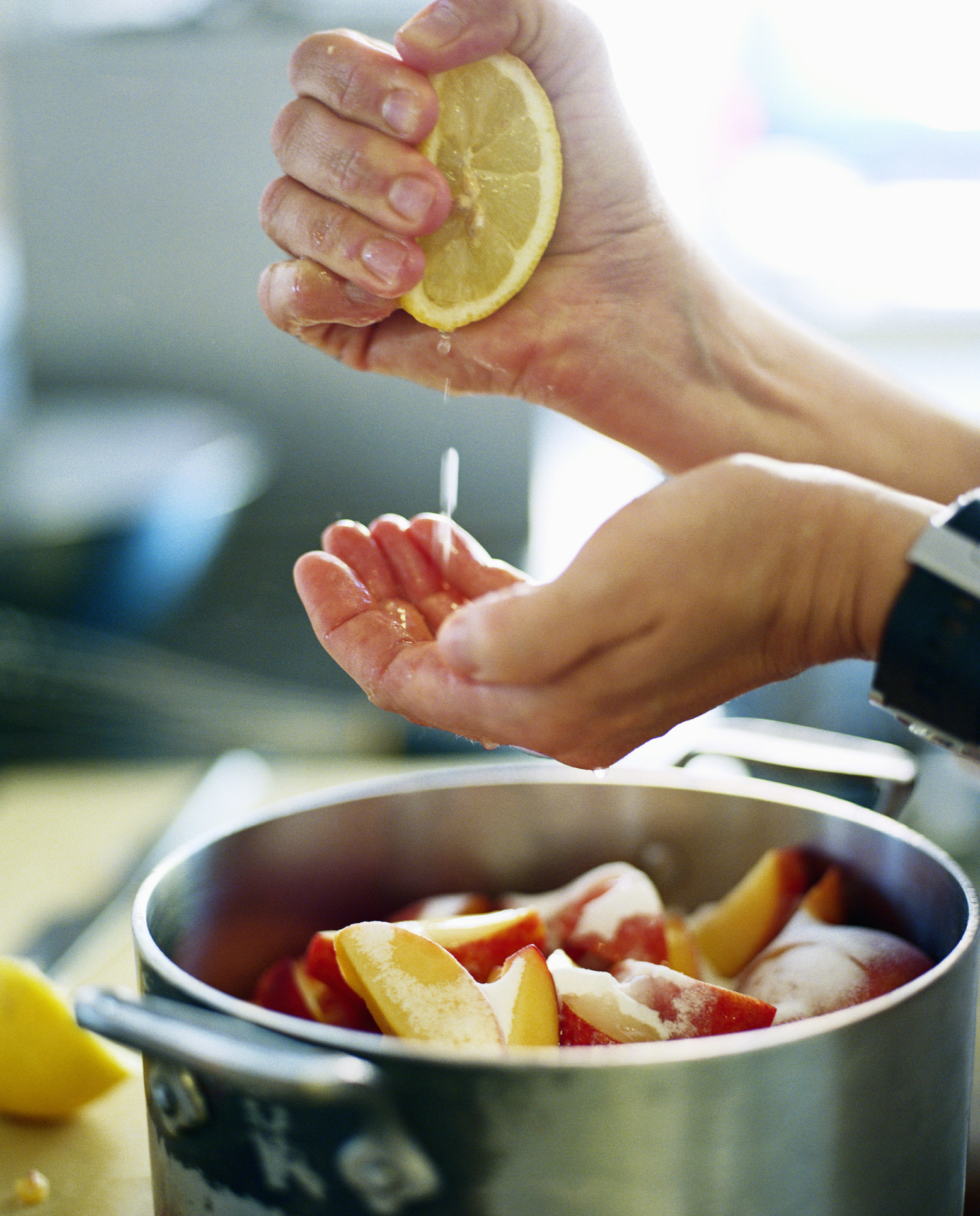 Someone squeezing a lemon into a pot of peaches.