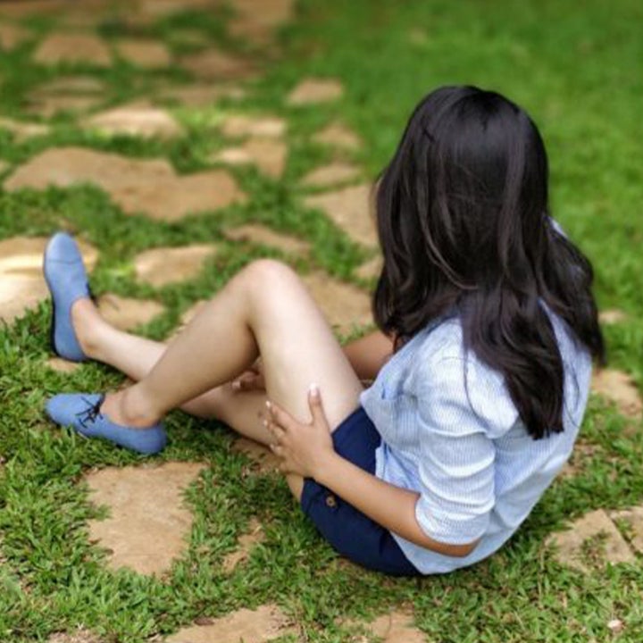 a model sitting in the grass wearing shorts, a shirt and the chambray blue lace-up shoes