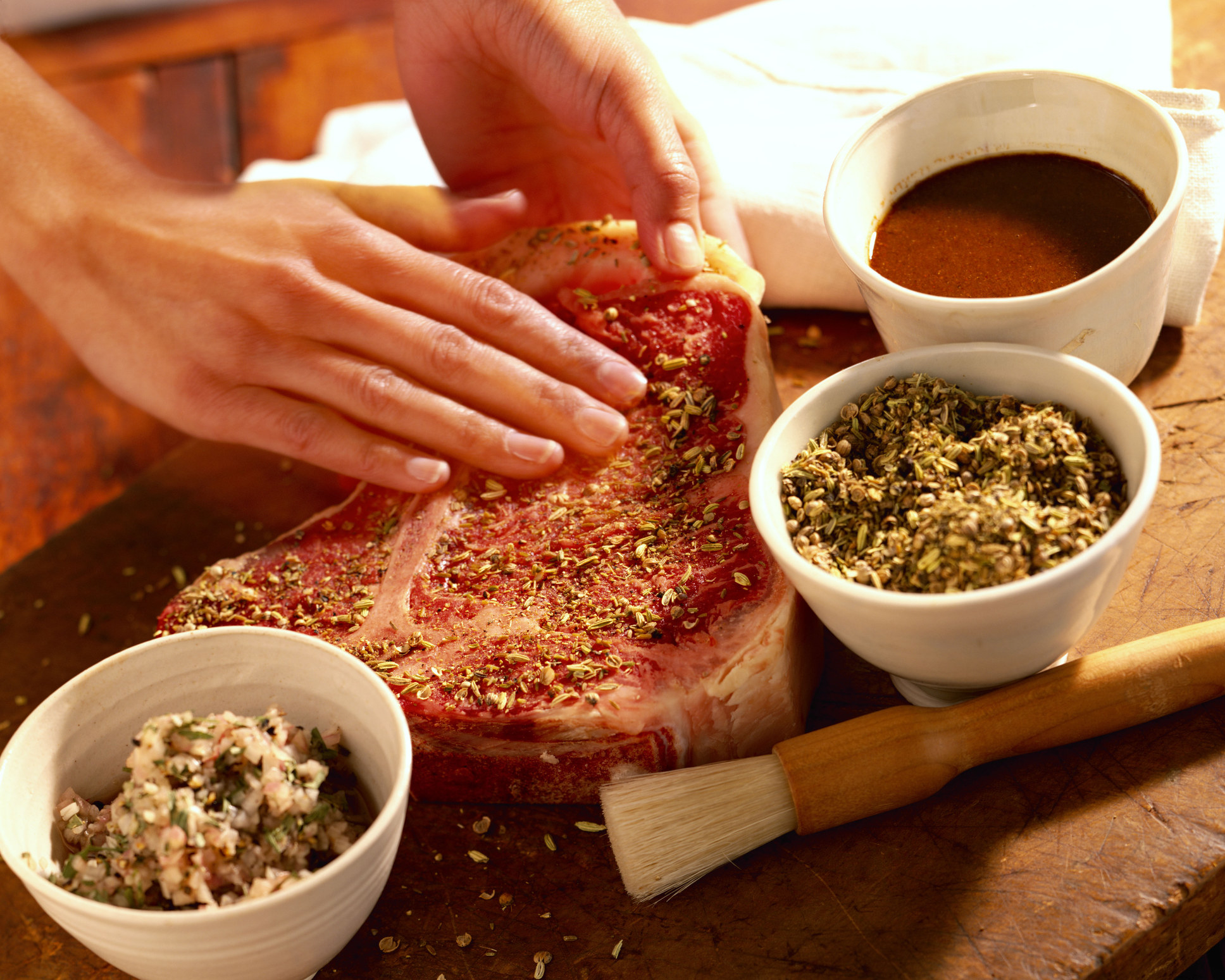Hands seasoning a steak with herbs. 