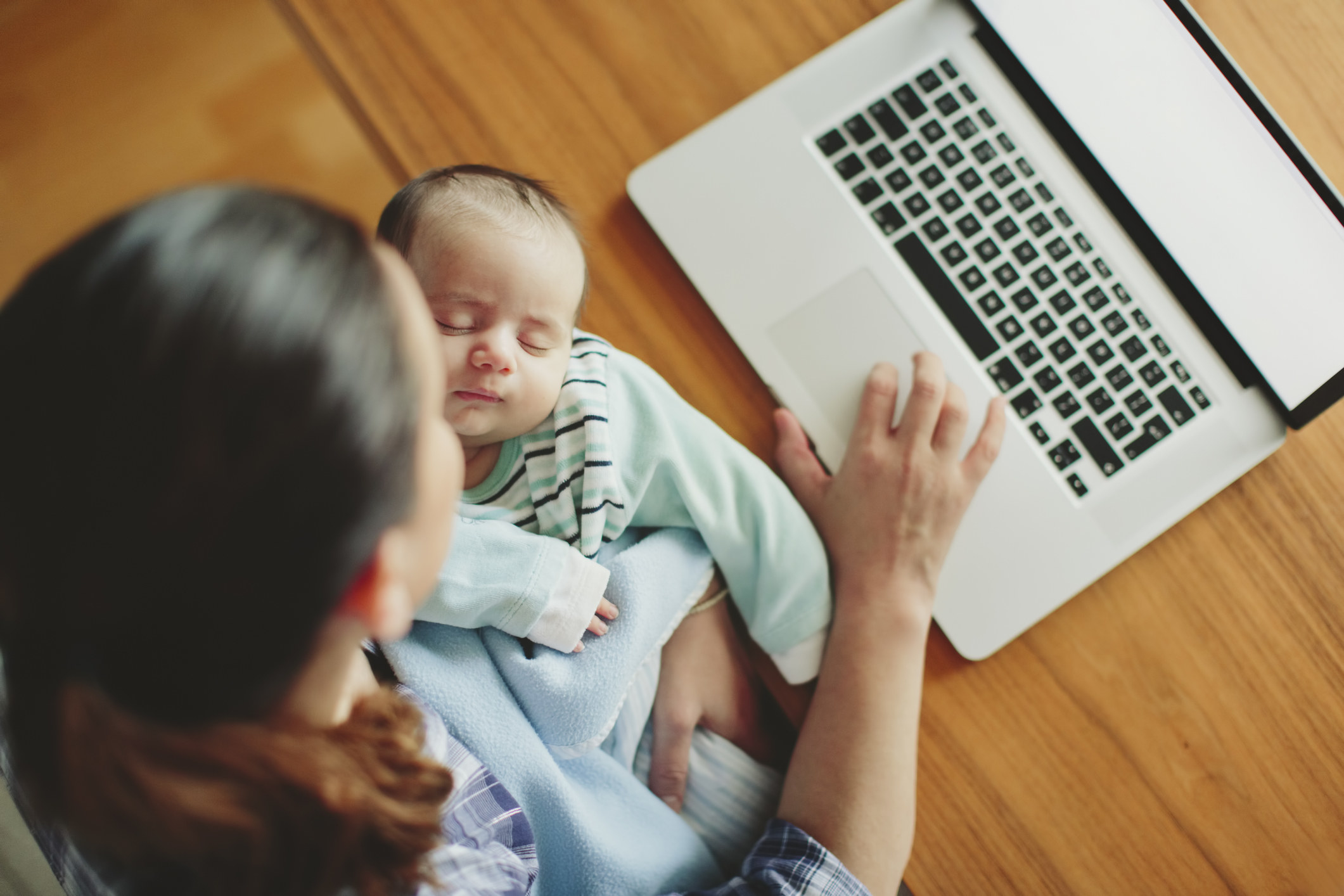 A mom holds her baby while working on a computer