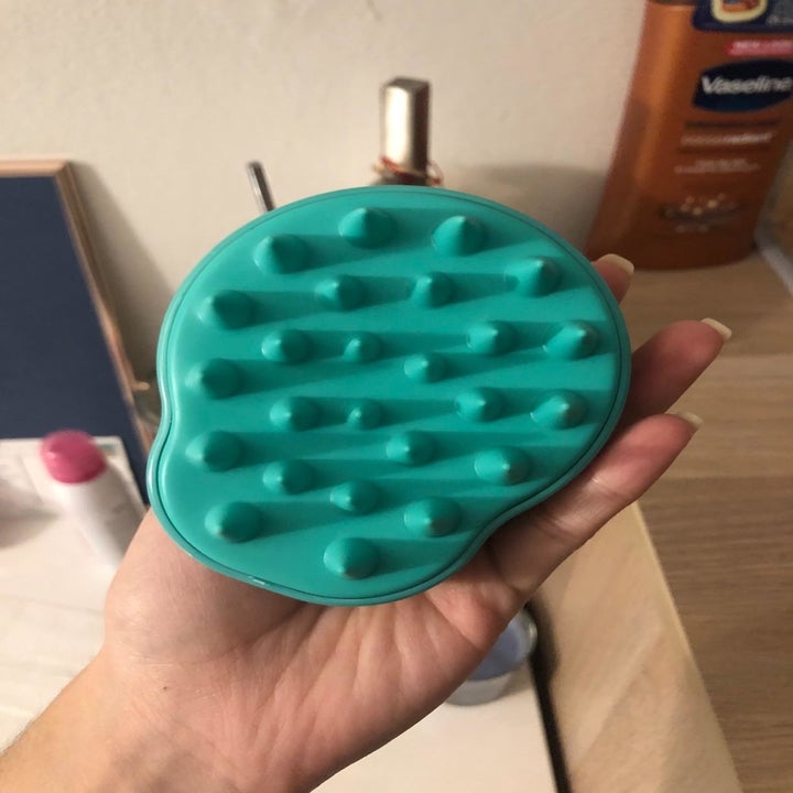 reviewer holds same green scalp massager in hand