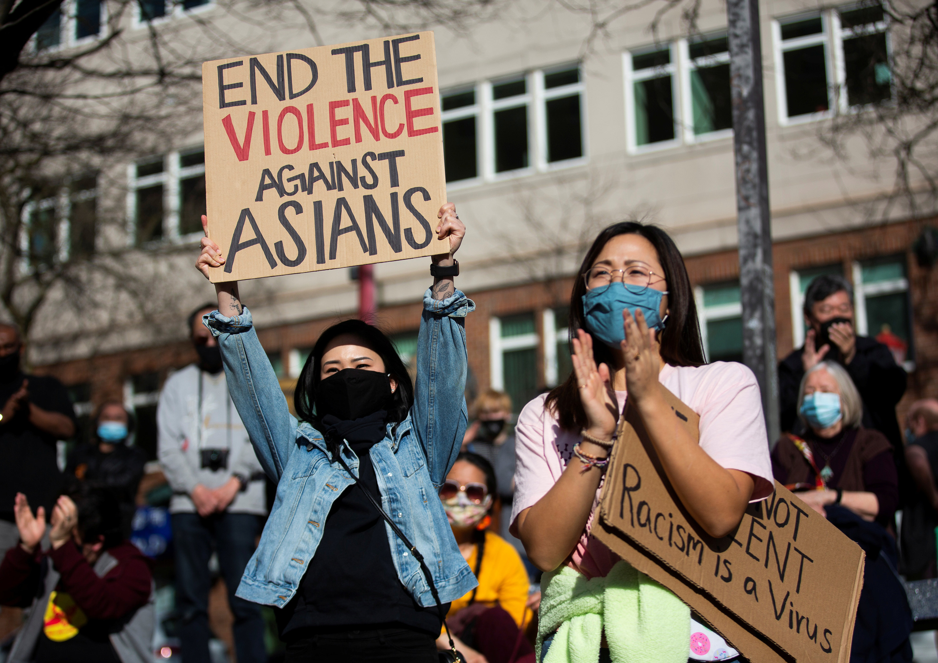 Two women in masks hold signs reading &quot;end the violence against Asians&quot; and &quot;racism is a virus&quot; at a protest