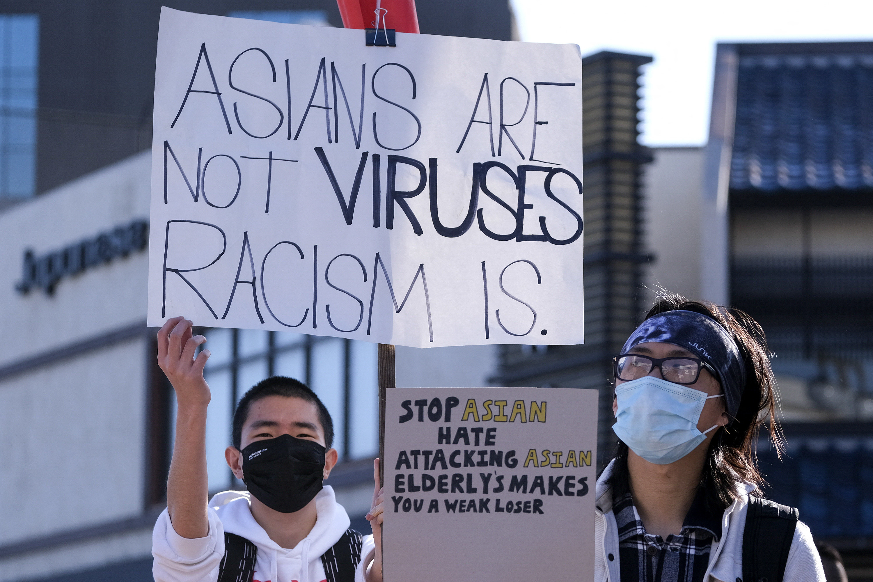 A man holds a sign reading &quot;Asians are not viruses, Racism is&quot; while a woman holds a sign reading &quot;stop Asian hate, attacking Asian elderlies makes you a weak loser&quot;