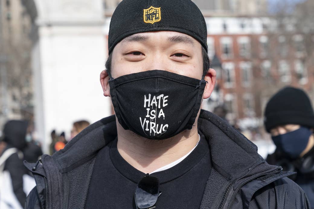 An Asian American man wears a mask that reads &quot;Hate is a virus&quot;