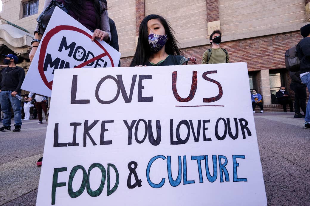A girl wearing a face mask holds a sign saying "love us like you love our food and culture"