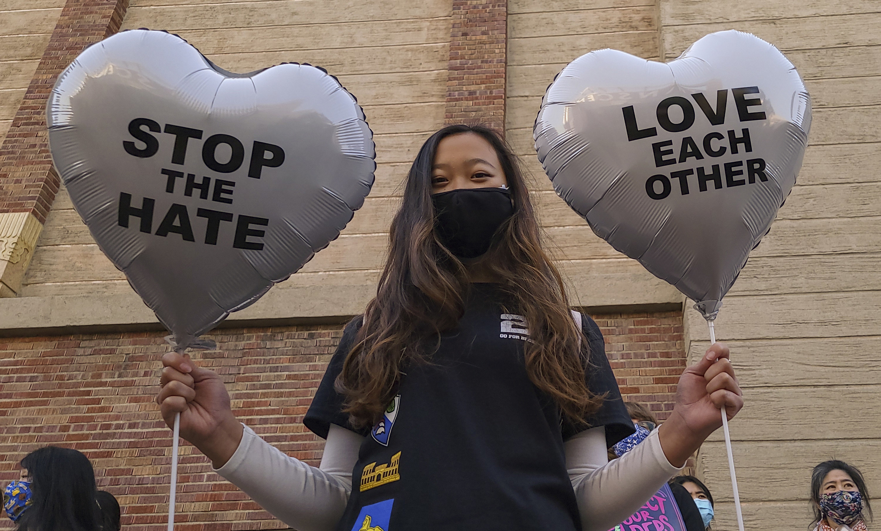 A woman holds two heart-shaped balloons that read &quot;stop the hate&quot; and &quot;love each other&quot;