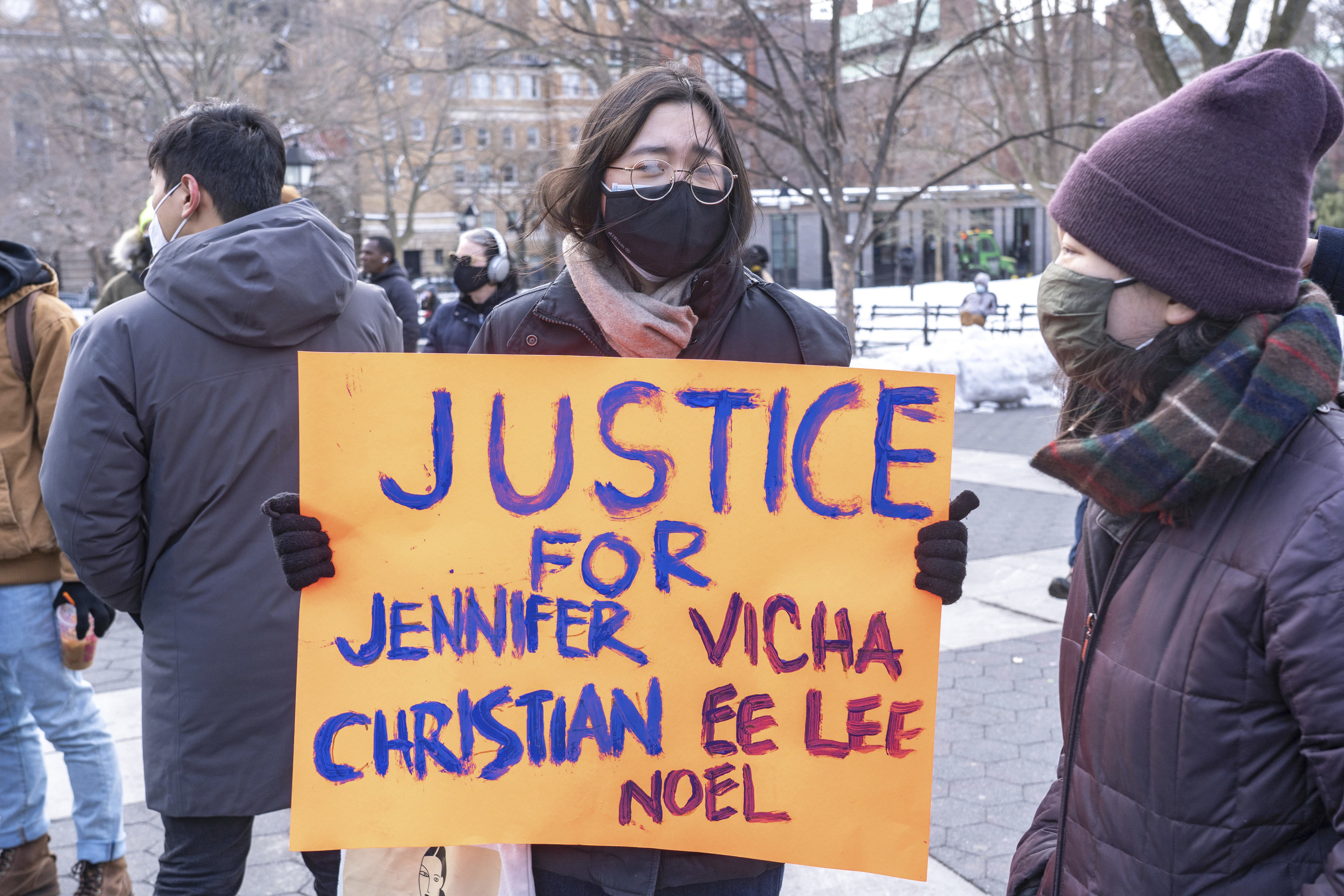 A protester wearing gloves, a jacket, scarf, and face mask holds a placard that reads &quot;justice for Jennifer Christian Vicha Ee Lee Noel&quot; during a demonstration