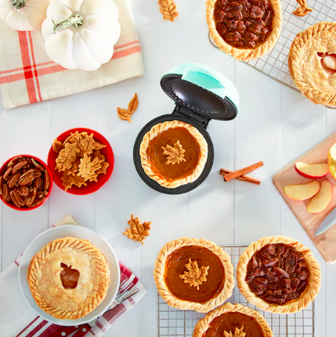 A flatlay of a small pie maker next to several dessert pies