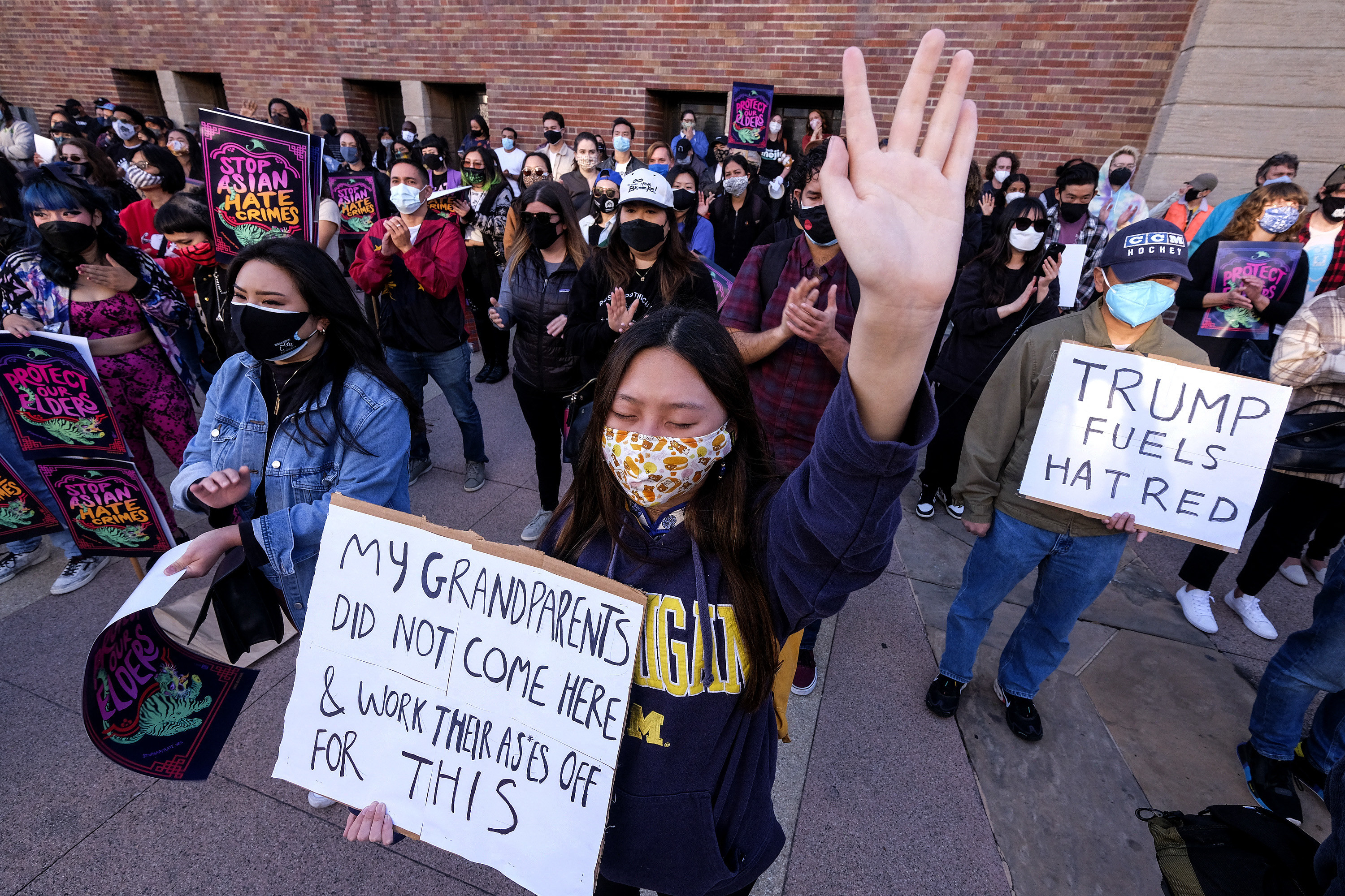 A woman holds a hand high in the air and carries a sign reading &quot;My grandparents did not come here and work their asses off for this&quot;
