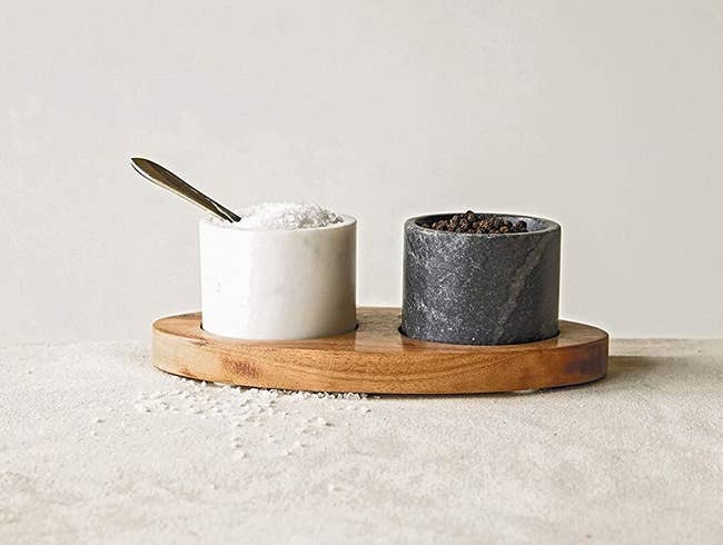a black and white marble bowl resting on a wooden tray with salt and pepper in each bowl