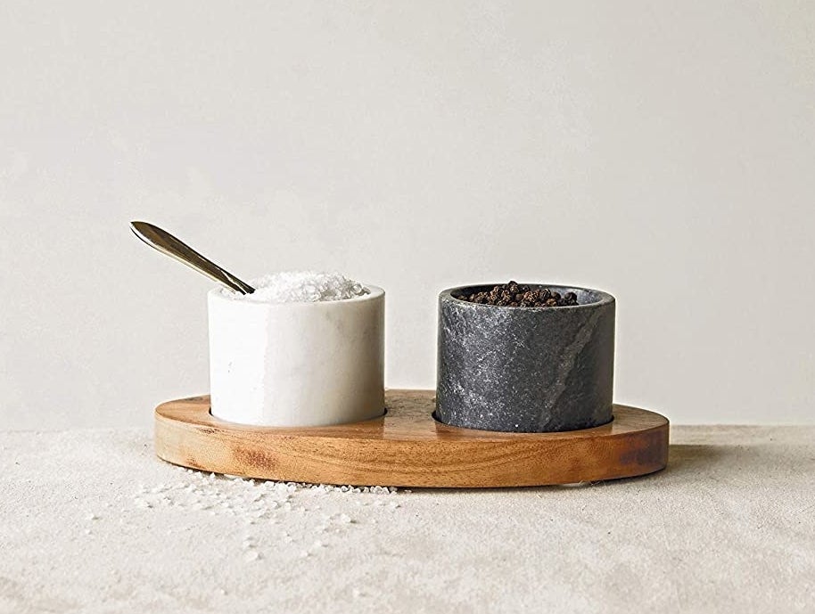 a black and white marble bowl resting on a wooden tray with salt and pepper in each bowl