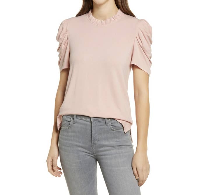 Model is wearing a blush pink top with ruffled sleeves and grey denim jeans