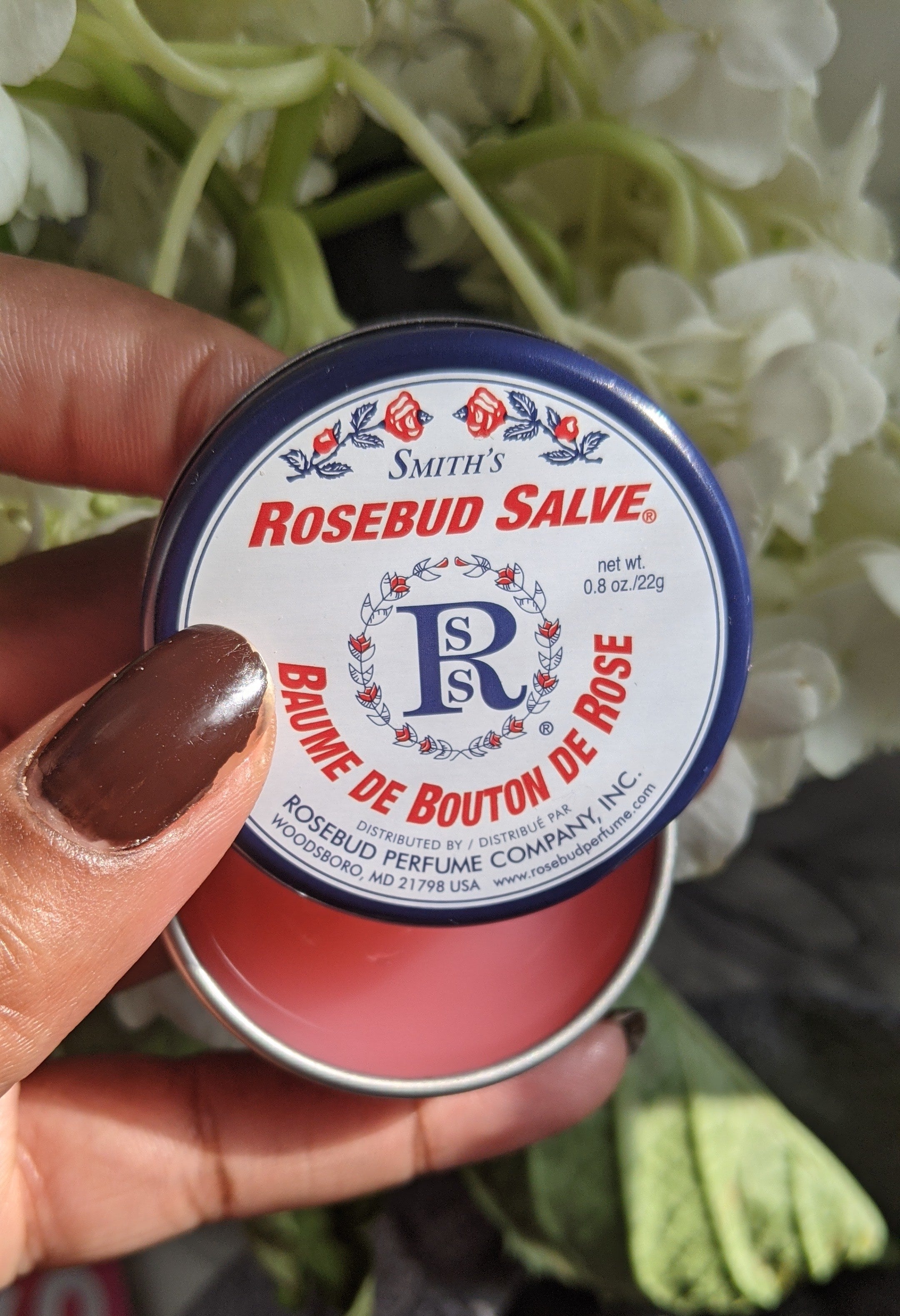 A person's hand holding a small tin of lip salve