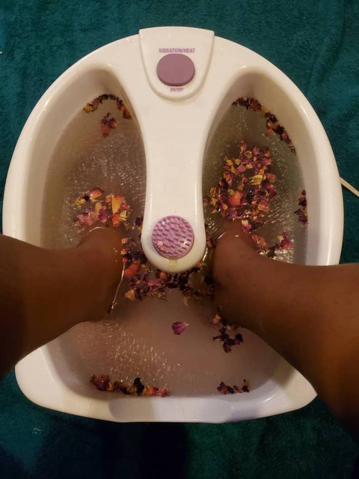 Feet inside foot bath with rose petals and product inside water 