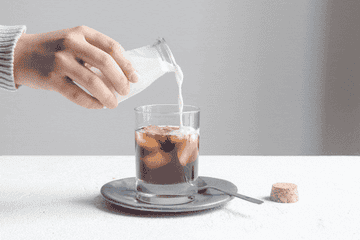 A GIF of someone pouring milk into a glass cup with black coffee