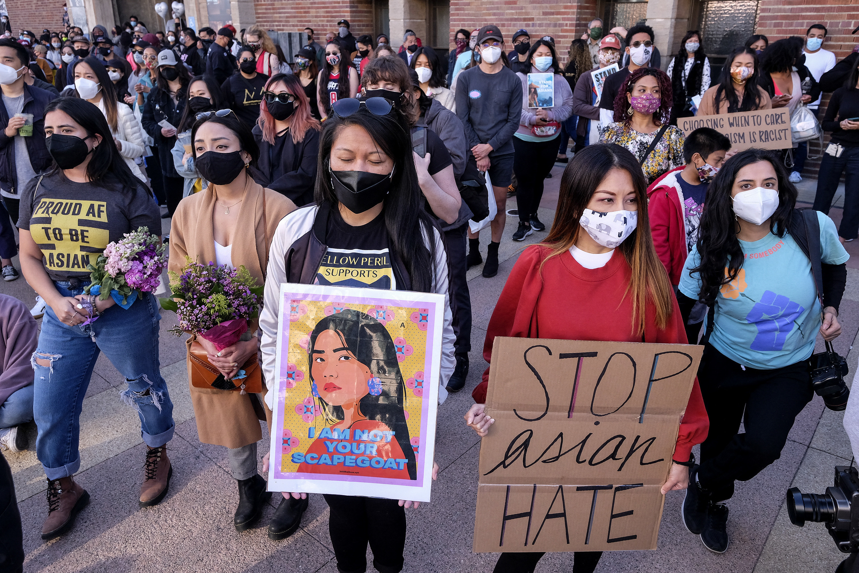 Two women in front of a large crowd hold signs reading &quot;stop Asian hate&quot; and &quot;I am not your scapegoat&quot; at a rally