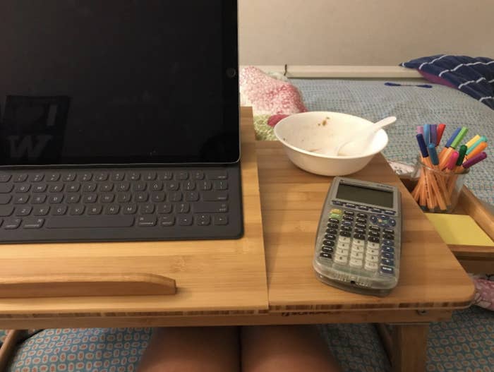 reviewer pic of them using the lap desk with a laptop, calculator, and bowl on the desk top 