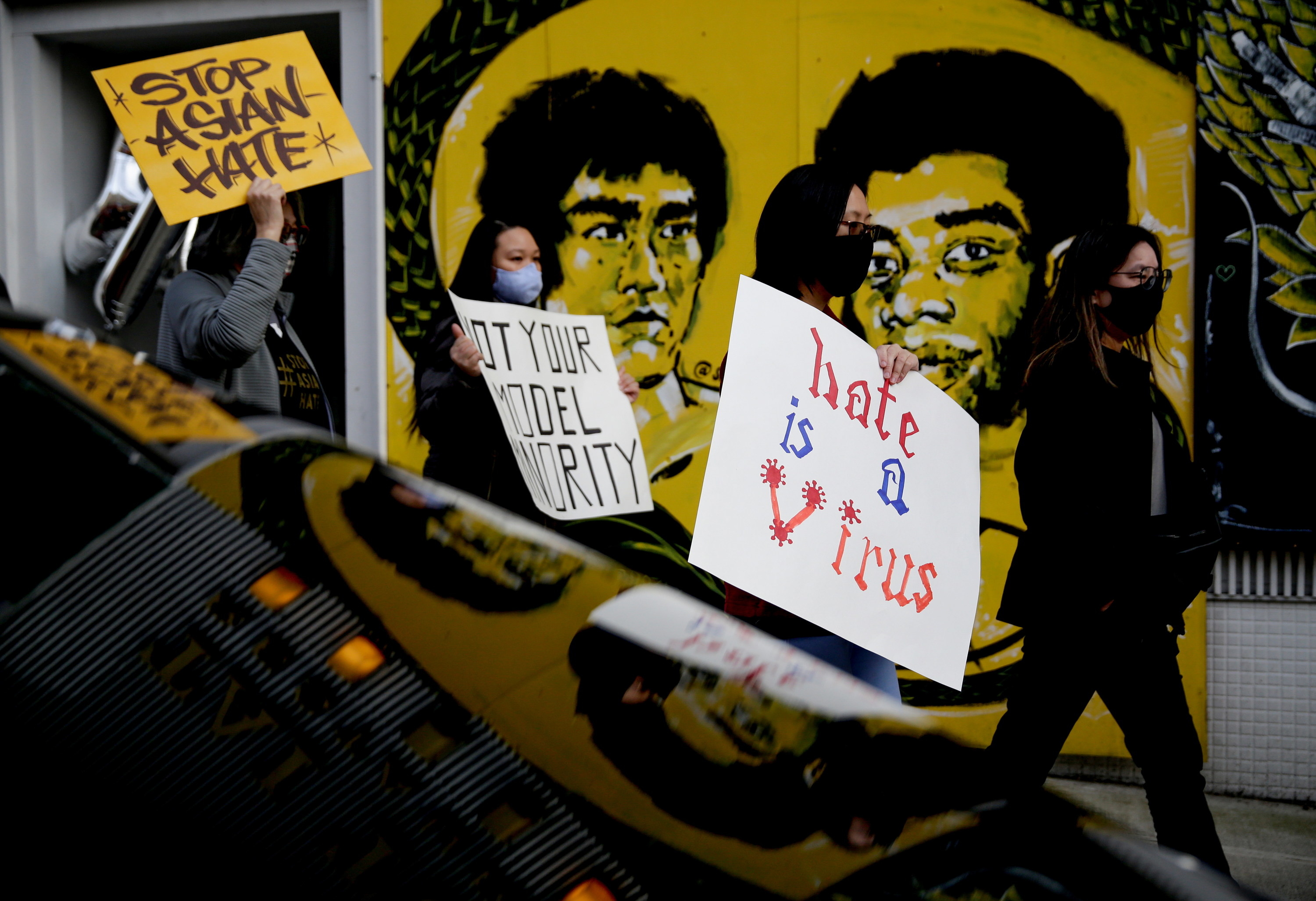 Three people walk by a mural of Bruce Lee with signs that read &quot;hate is a virus&quot; and &quot;stop Asian hate&quot;