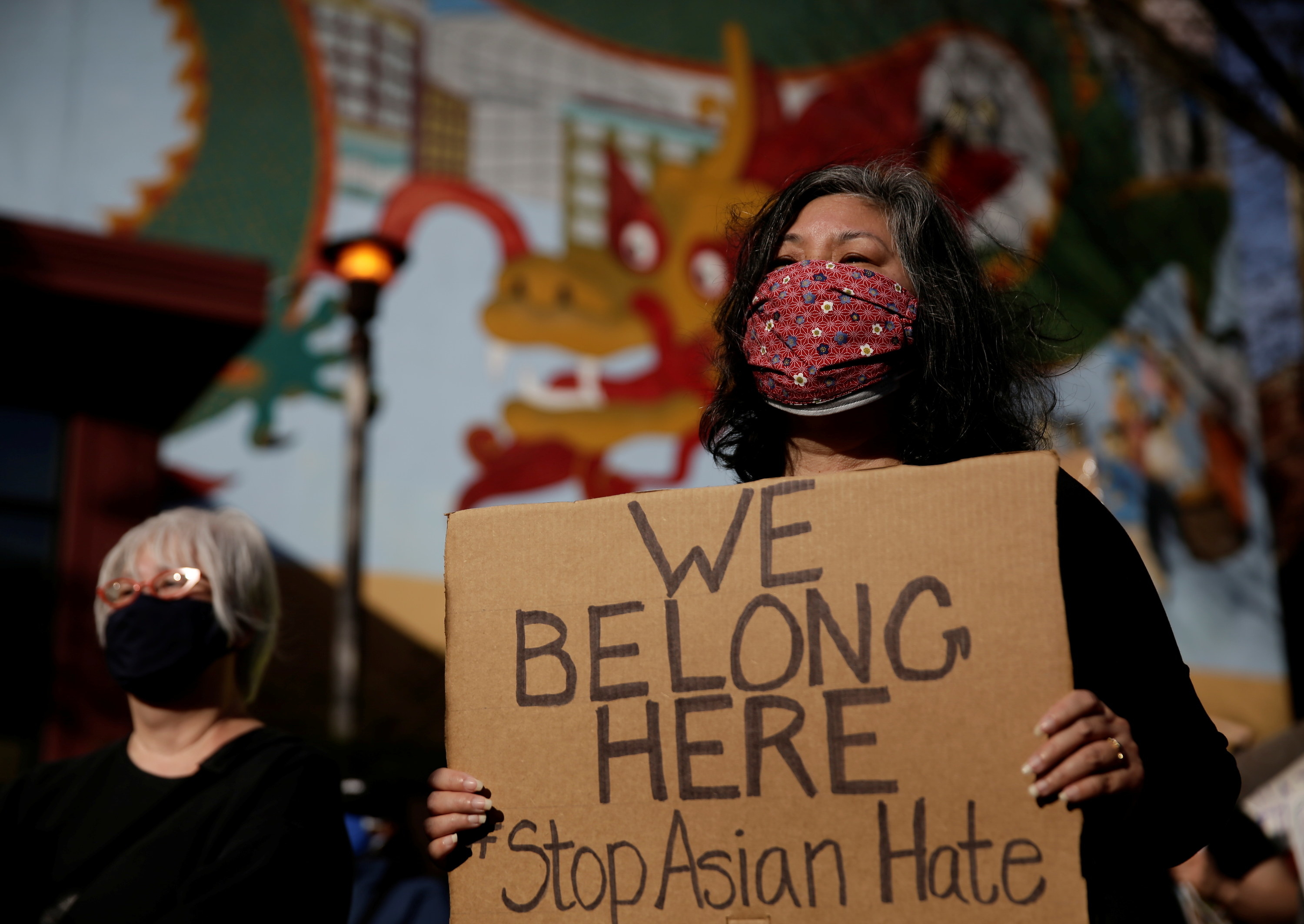 a woman holds a sign that reads &quot;We Belong Here, Stop Asian hate&quot;