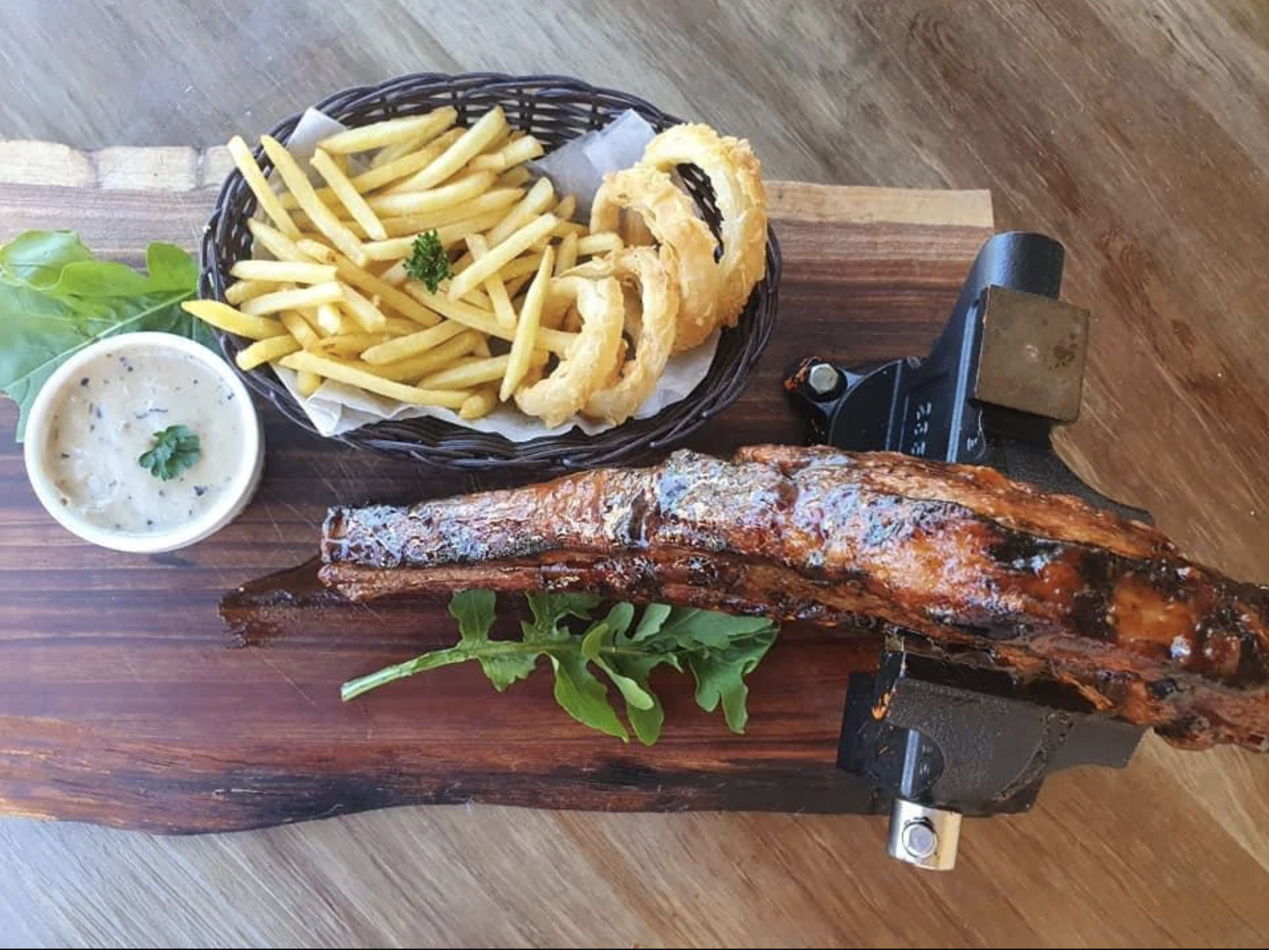 Steak served in a vice with fries and onion rings on a board