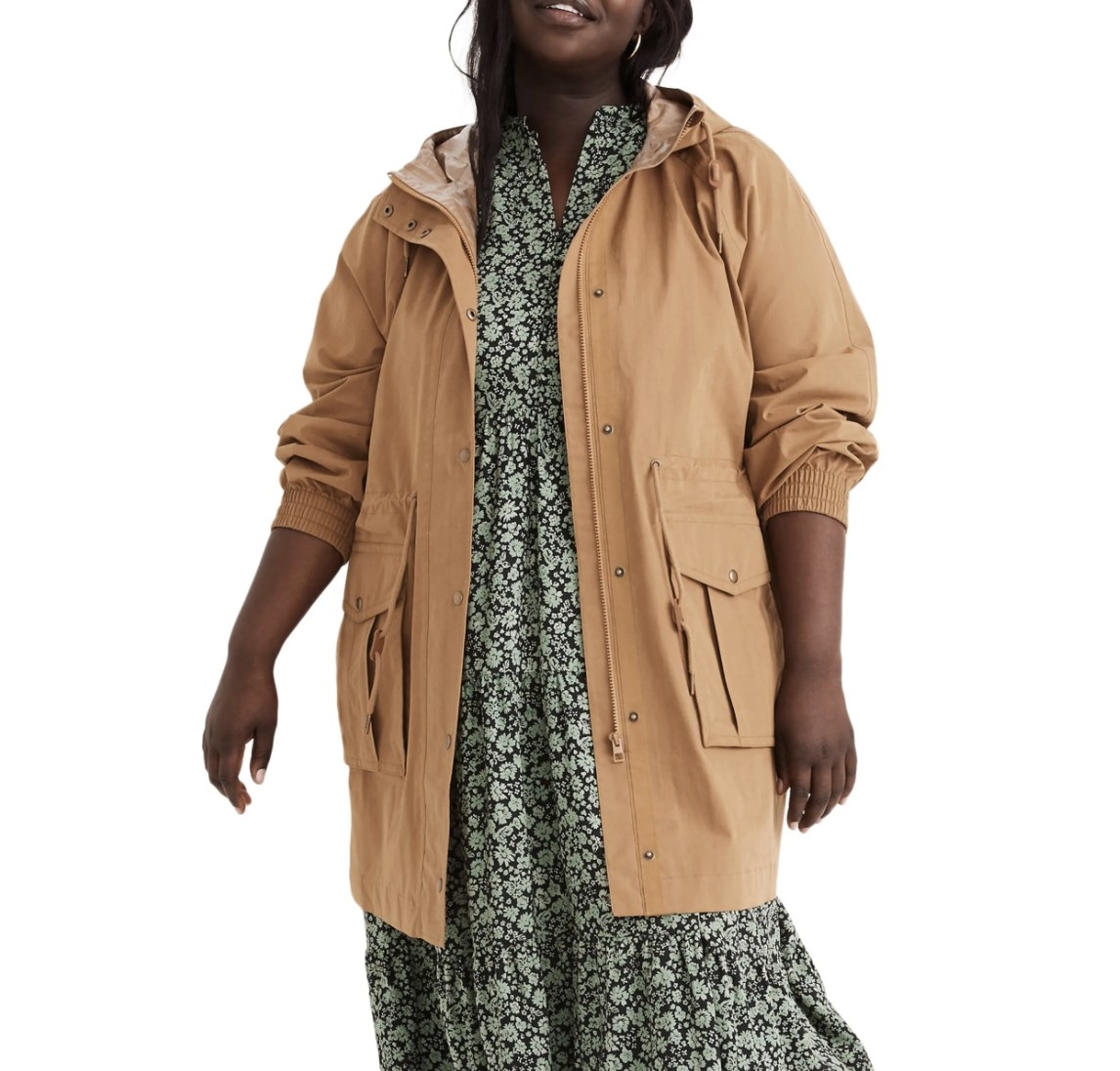 Model is wearing a beige raincoat over a green floral dress