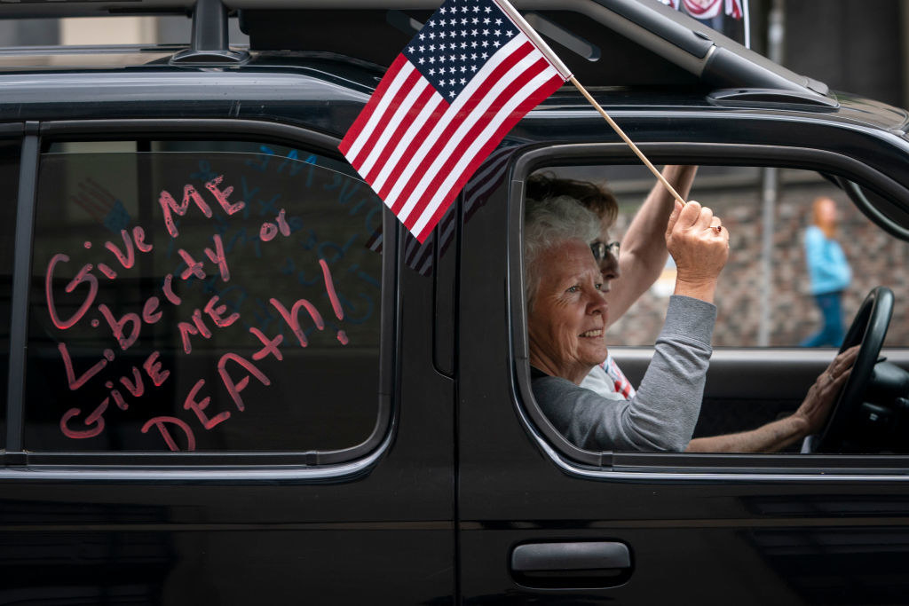 Older woman in the passenger seat of a truck and waving an American flag with the words "Give me liberty or give me death!" on the car window behind her