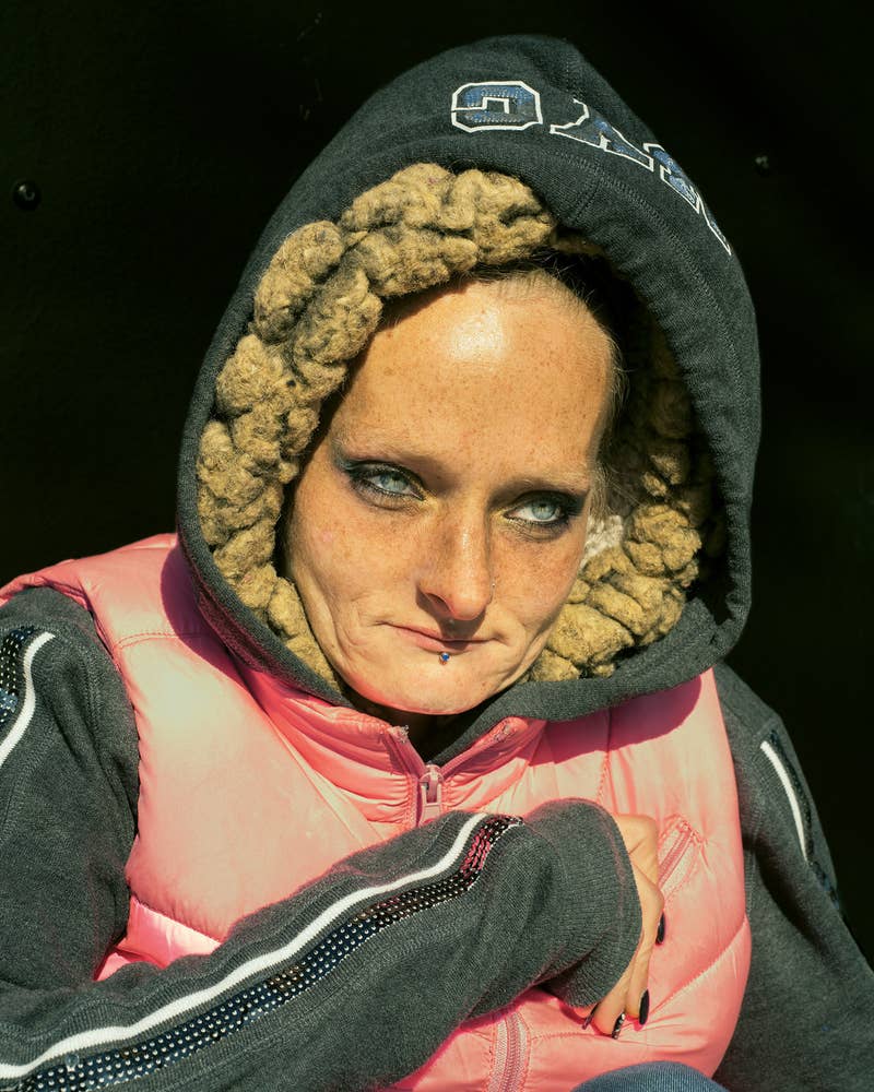 A woman in a hoodie and vest curls up into herself, looks out past the camera