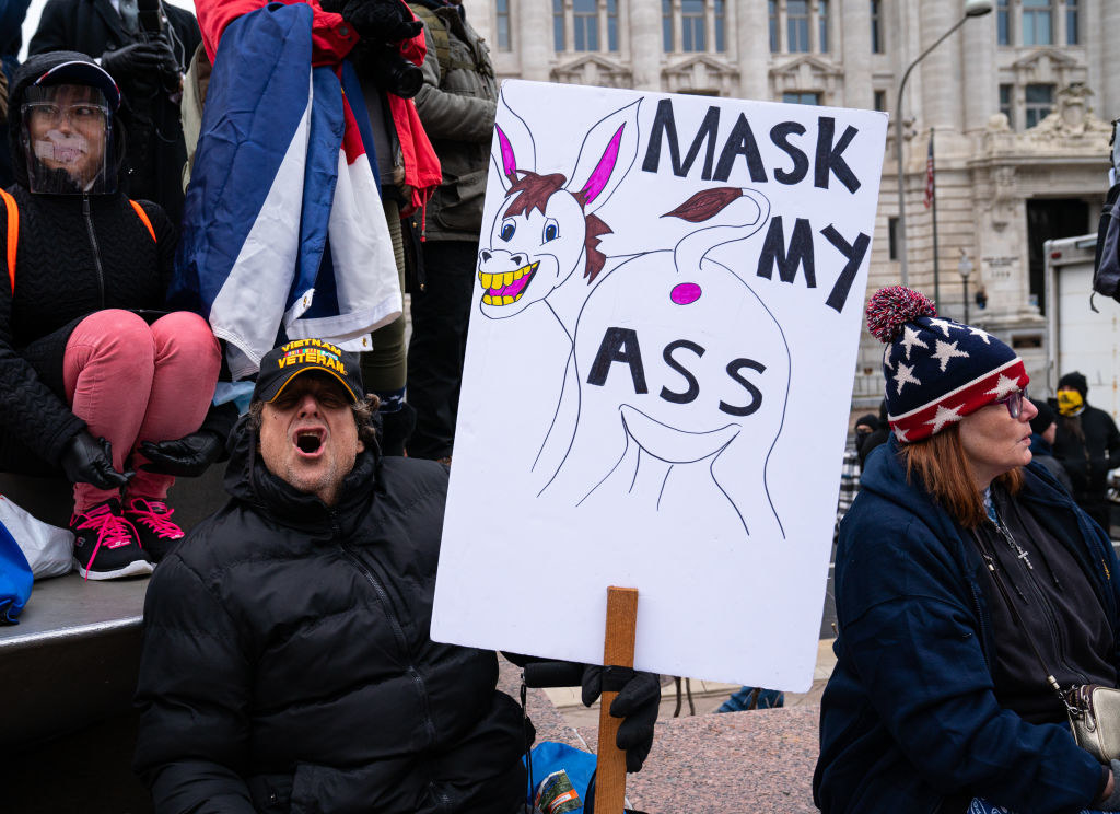 Man holding a sign reading, &quot;Mask my ass&quot; and showing the rear end of a donkey
