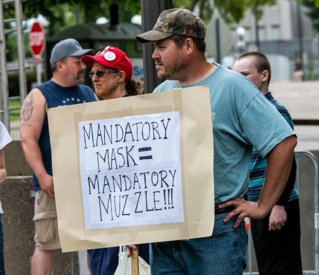 Man wearing a cap and holding a sign reading, &quot;Mandatory mask = mandatory muzzle!!!&quot;