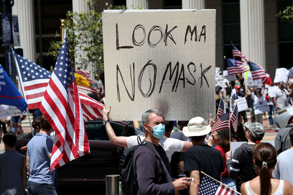 Person in a crowd of protesters holding up a sign reading, "Look Ma no mask"