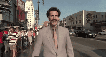 a gif of Sacha Baron Cohen in &quot;Borat&quot; walking down the street, smiling 