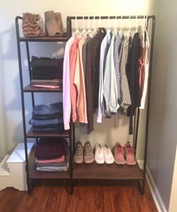 reviewer's black garment rack with hanging clothes, folded clothes, and shoes