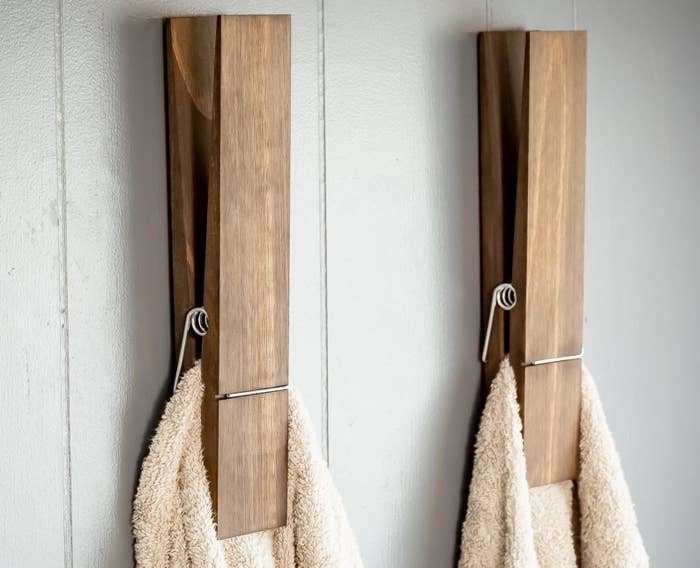 two jumbo clothespin towel holders mounted to a wall, each holding a beige towel