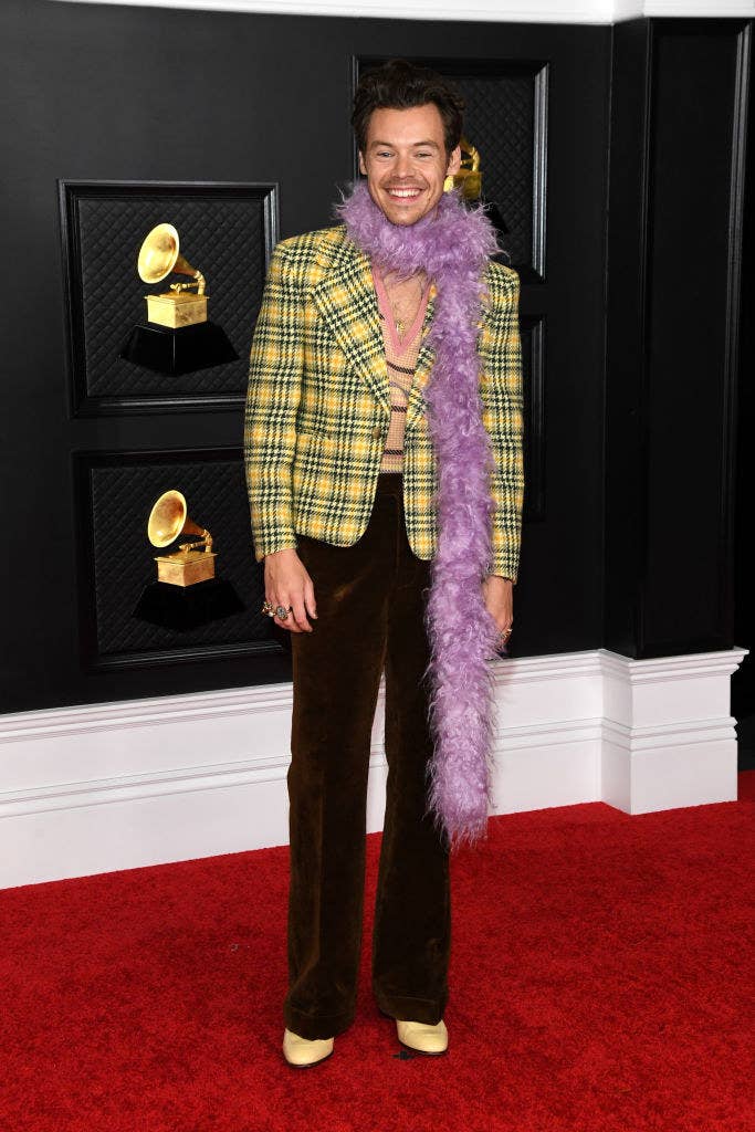 Harry wearing a plaid blazer and a feather boa as he smiles on the Grammys red carpet