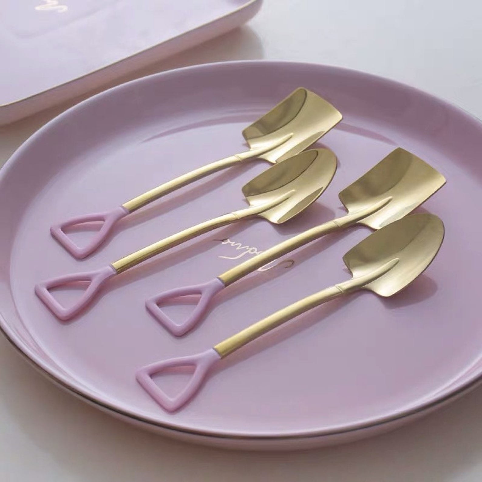 four pink and gold shovel spoons on a pink plate