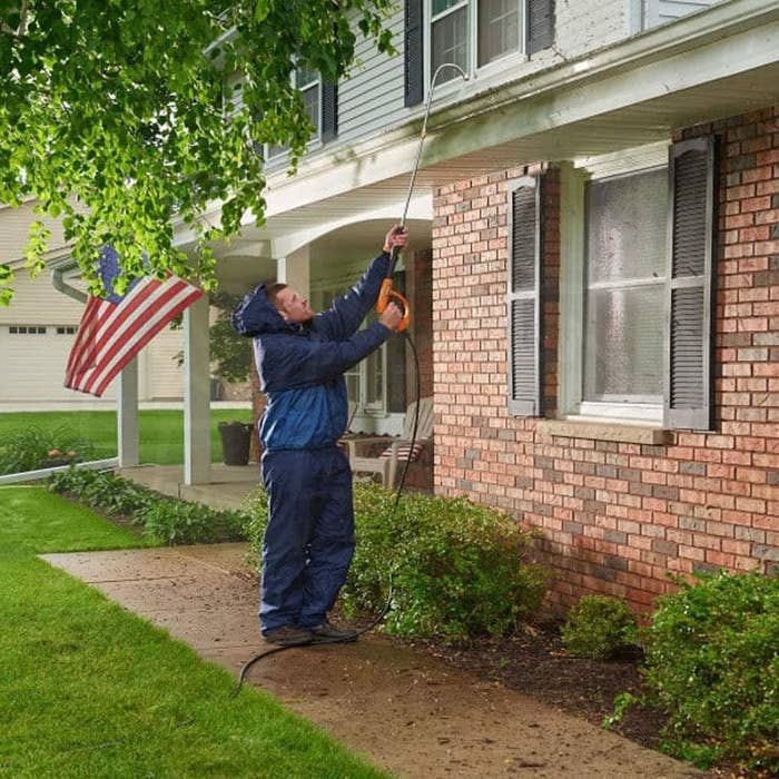 Person standing on the ground cleaning their gutters using the curved tube attached to a pressure washer to clean gutters
