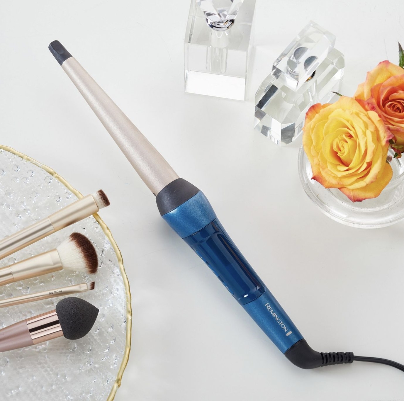 A blue curling wand, makeup brushes, and flowers