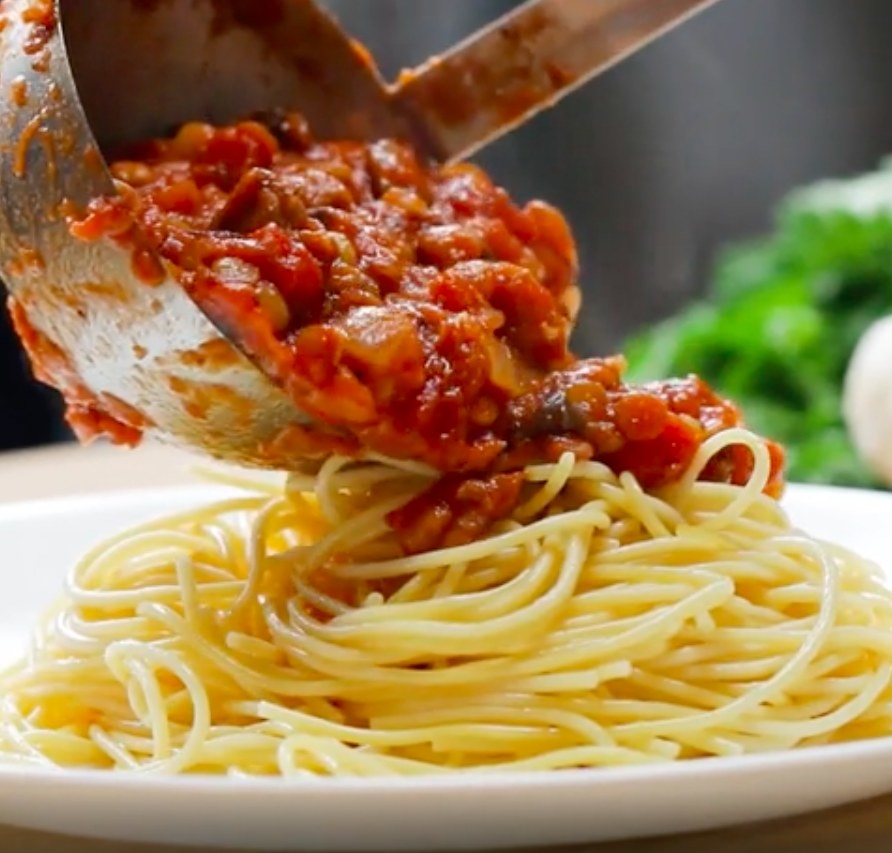 The Bolognese being served on top of a plate of spaghetti