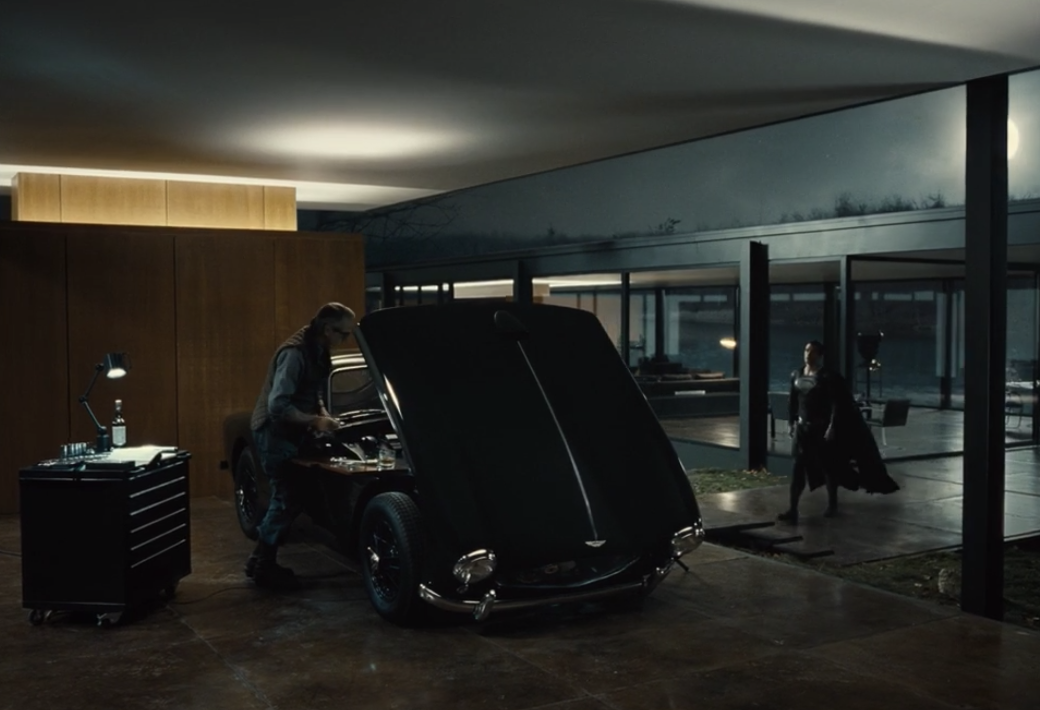 Alfred working on a car as Superman walks up